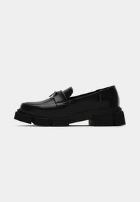 Black leather loafers with a chunky, textured sole. Features a flat, rounded toe and a front strap detail. Smooth finish and minimal stitching.