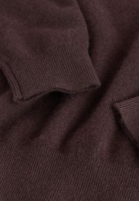 Brown knit sweater fabric, featuring a soft texture, ribbed cuffs, and a slightly fuzzy surface. No distinct patterns or accents present.