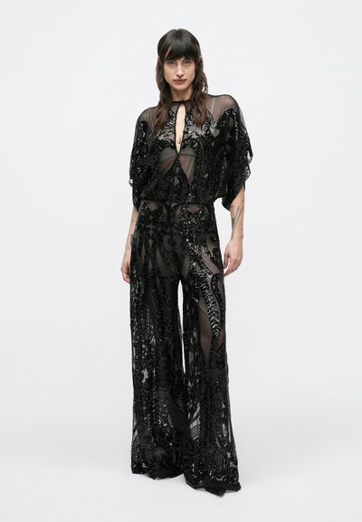 Fekete átlátszó overall részletes gyöngyözéssel és hímzéssel. Széles ujjak, mély kivágás és könnyed, bő szabás jellemzi.