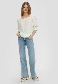 Blouse blanche texturée avec un décolleté carré et des manches bouffantes, associée à un jean clair à jambes larges et des sandales à plateforme beiges.