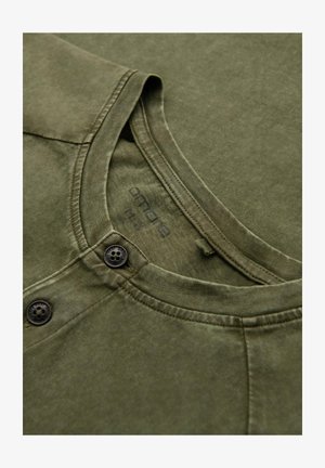 Olijfgroene katoenen t-shirt met een ronde hals, twee knoopsluitingen en zichtbare stikseldetails. Zachte, gestructureerde stof.