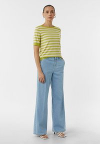 Jasnozielona bluzka w białe paski z krótkim rękawem w połączeniu z szerokimi, jasnoniebieskimi dżinsami oraz białymi sandałami na obcasie. Prosty krój, swobodny styl.