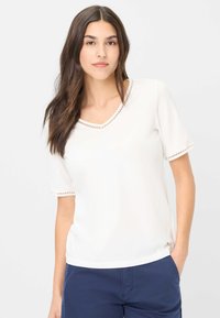 Witte v-hals top met korte mouwen, voorzien van decoratieve stiksels langs de halslijn en mouwzoom. Zacht materiaal en comfortabele pasvorm.