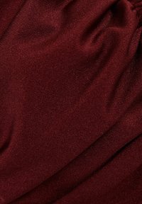 Artimas minkštos, raukšlėtos tamsiai bordo spalvos audinio vaizdas su smulkiu briaunotu raštu ir subtiliomis šviesos atspindėjimo žaismėmis.