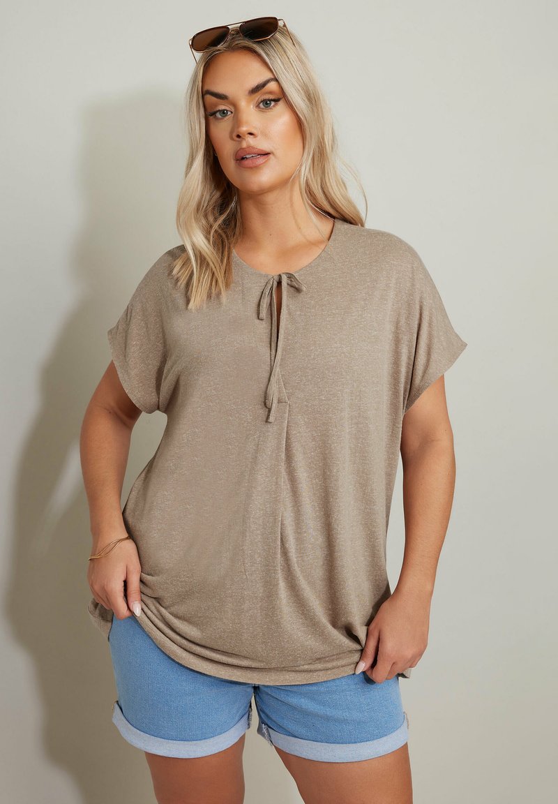 Top beige a maniche corte con scollo rotondo e dettaglio con fiocco, abbinato a pantaloni corti in denim azzurro chiaro con risvolti. Texture liscia.