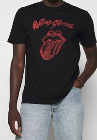Czarny bawełniany t-shirt z wyblakłym czerwonym logo Rolling Stones i ikoniczną grafiką języka z przodu. Krótkie rękawy, okrągły dekolt.