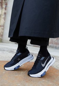 Czarne sneakersy Nike z teksturowaną cholewką, białą podeszwą i widoczną poduszką powietrzną. Posiadają widoczne logo swooshu oraz sznurowany fason.