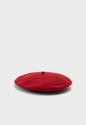 Klassisk rød uld-baret med en lille stilk på toppen, placeret fladt på en lys grå baggrund.