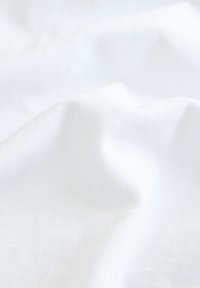 Tessuto di cotone bianco con una superficie liscia e strutturata, che mostra pieghe e increspature sottili. Nessun motivo o accento distintivo visibile.