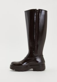 Bota de lluvia negra brillante y alta con suela gruesa y cremallera lateral, diseñada para uso impermeable.