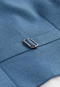 Gros plan sur un tissu bleu avec un tissage texturé. Présente un détail de boucle métallique fixé à une sangle. Fini lisse avec un doux éclat.
