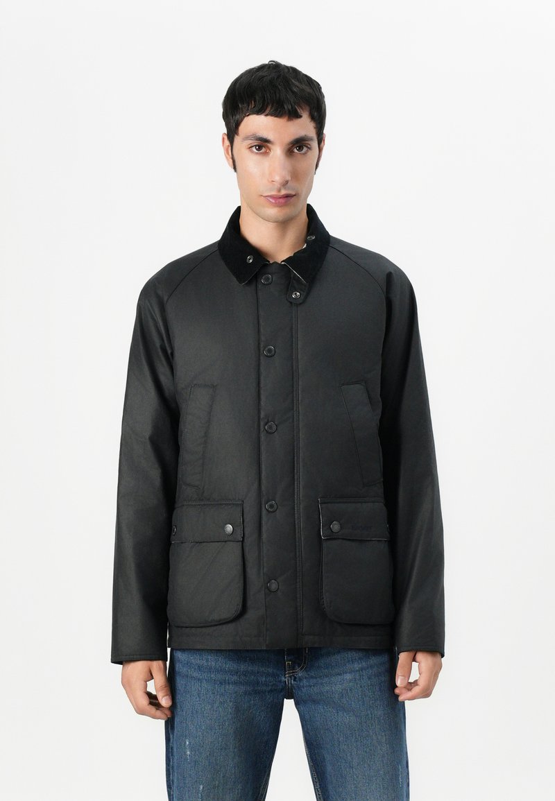 Veste noire en matériau lisse, avec un col, une fermeture à boutons et deux poches avant. Accents texturés sur le col.