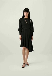 Schwarzes Kleid mit asymmetrischem Saum, langen Ärmeln und Cutout-Detail. Aus weichem Stoff gefertigt, hat es eine taillierte Taille und eine fließende Silhouette.