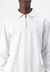 Grijze langemouwen polo-shirt gemaakt van zachte stof, met een ritsnek en klassiek kraagontwerp.