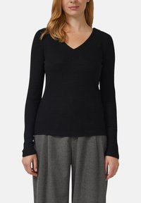 Czarna prążkowana bluzka z długim rękawem i dekoltem w kształcie litery V. Gładka faktura, dopasowany krój i delikatne rozszerzenie u dołu, zestawiona z szarymi spodniami o szerokich nogawkach.