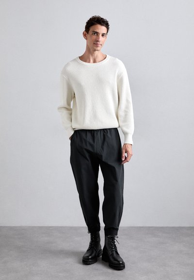 Valkoinen ribattu neule, mustat elastiset vyötäröhousut ja mustat nauhakenkä. Yksinkertainen muotoilu, jossa on teksturoitu materiaali ja rento istuvuus.