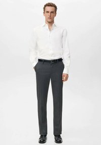 Biała koszula zapinana na guziki w zestawieniu z ciemnoszarymi spodniami wizytowymi. Strój uzupełnia czarny pasek i błyszczące czarne buty, tworząc formalny wygląd.