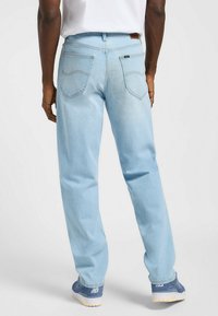 Vaqueros de denim azul claro con corte recto, que cuentan con dos bolsillos traseros y costuras en contraste. Llevados con zapatillas azules.