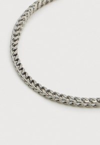 Ασημένιο κολιέ αλυσίδας με πλεκτό σχέδιο, λεία υφή και ομοιόμορφους συνδέσμους, που αντανακλά το φως με γυαλιστερό φινίρισμα.