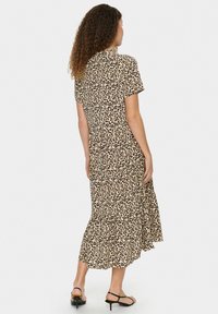 Robe midi à imprimé léopard en beige et noir, avec des manches courtes, une jupe à volants et une coupe décontractée. Fini avec une texture douce.