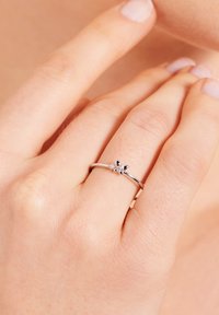 Silver ring with a floral design featuring a black accent and two small clear stones, worn on a hand with light skin tone and neutral nail polish.