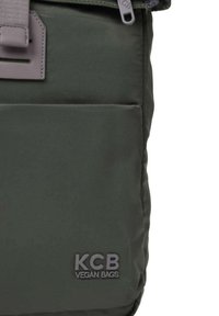 Donkergroene vegan tas van een textuurstof, met een voorvak en een grijze band. KCB-logo gedrukt op de lagere voorkant.