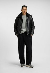 Giubbotto in pelle nera con colletto in shearling, maglione grigio a maglia texture, pantaloni neri e sneakers grigie. Design semplice e moderno.