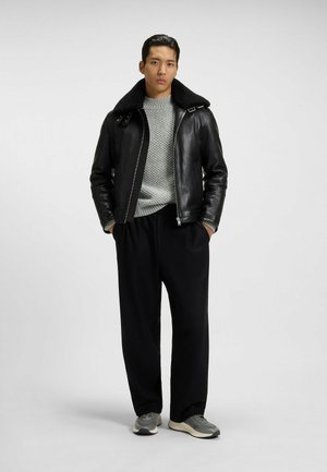 Schwarze Lederjacke mit einem Lammfellkragen, grauer strukturierten Strickpullover, schwarze Hose und graue Turnschuhe. Einfaches, modernes Design.