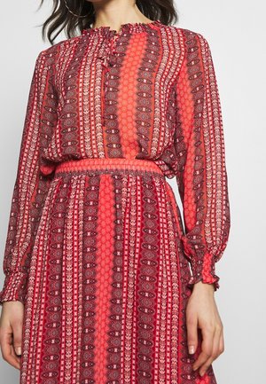 Robe à motifs rouges en tissu fluide, avec un haut de style blouse doté d'un col volanté et de manches longues, une taille cintrée et des motifs floraux.