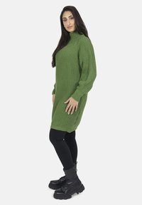 Abito di maglia a coste verde con collo alto, maniche lunghe e spacchi laterali, abbinato a leggings neri e stivali neri chunky con lacci.