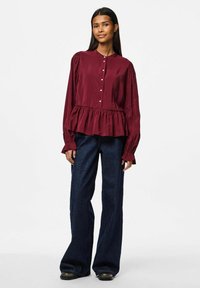 Bordeaux långärmad blus med peplummidja, knappar framtill och samlade ärmar. Kombination med mörka utsvängda jeans och svarta skor.