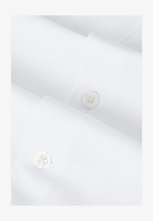 Gros plan sur des poignets de chemise blancs avec des boutonnières cousues et des boutons en plastique blanc dans un éclairage lumineux et doux.