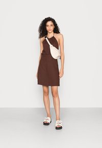 Vestido castanho com alças, com cintura franzida, combinado com uma bolsa crossbody beige e sandálias brancas com soles pretos. Textura suave, design simples.