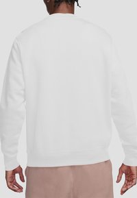 A person wearing a white sweatshirt stands sideways, showcasing the back of the garment against a neutral background.
