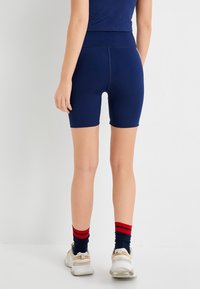 Mallas de ciclismo azul marino con una cintura alta, textura suave y un diseño ajustado. Combinadas con zapatillas blancas y calcetines azul marino con rayas rojas.