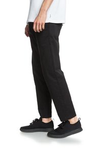 Zwart taps toelopende broek van een lichtgewicht stof, gecombineerd met zwarte mesh sneakers met platte veters en getextureerde zolen. Eenvoudig, modern ontwerp.