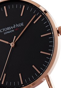 Reloj analógico en oro rosado con un dial negro, marcadores de hora minimalistas y agujas delgadas. Diseñado con una textura de cuero suave.