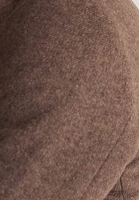 Brązowa teksturowana tkanina o gładkim, miękkim wykończeniu z delikatnym połyskiem. Materiał wydaje się gruby i ciepły, odpowiedni na odzież wierzchnią.