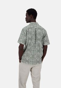 Camicia a maniche corte verde con un motivo floreale bianco, dotata di colletto button-down e vestibilità rilassata, abbinata a pantaloni beige chiaro.