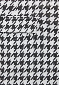 Svart och vit hounds-tooth-mönstrad tyg med en ficka. Texturen verkar vävd med en strukturerad design.