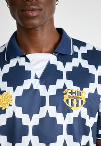 Marinblå och vit polo shirt med geometriskt mönster, broderade sol- och sköldlogotyper samt en klassisk krage. Texturerad tyg.