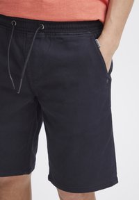 Mörkblå bomullsshorts med elastisk midja och dragsko, med sidofickor och en liten etikett nära höften.