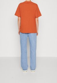 Rostfärgad t-shirt med kort ärm tillsammans med ljusblå vida jeans, har en avslappnad passform och enkel design.