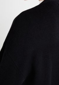 Czarny sweter dzianinowy o gładkiej teksturze, luźnym kroju i opuszczonych ramionach. Charakteryzuje się prostym designem, bez widocznych wzorów lub elementów hardware.