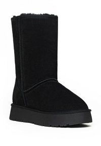 Botín negro de ante con suela de goma plana, forro suave y costuras visibles a lo largo de las costuras. Puntera redonda con altura hasta medio pantorrilla.