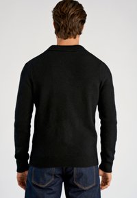 Czarny dziergany sweter z wysokim kołnierzem i ściągaczami na mankietach. Miękka tekstura, dopasowany krój i jednolity kolor. Noszony z niebieskimi dżinsami.