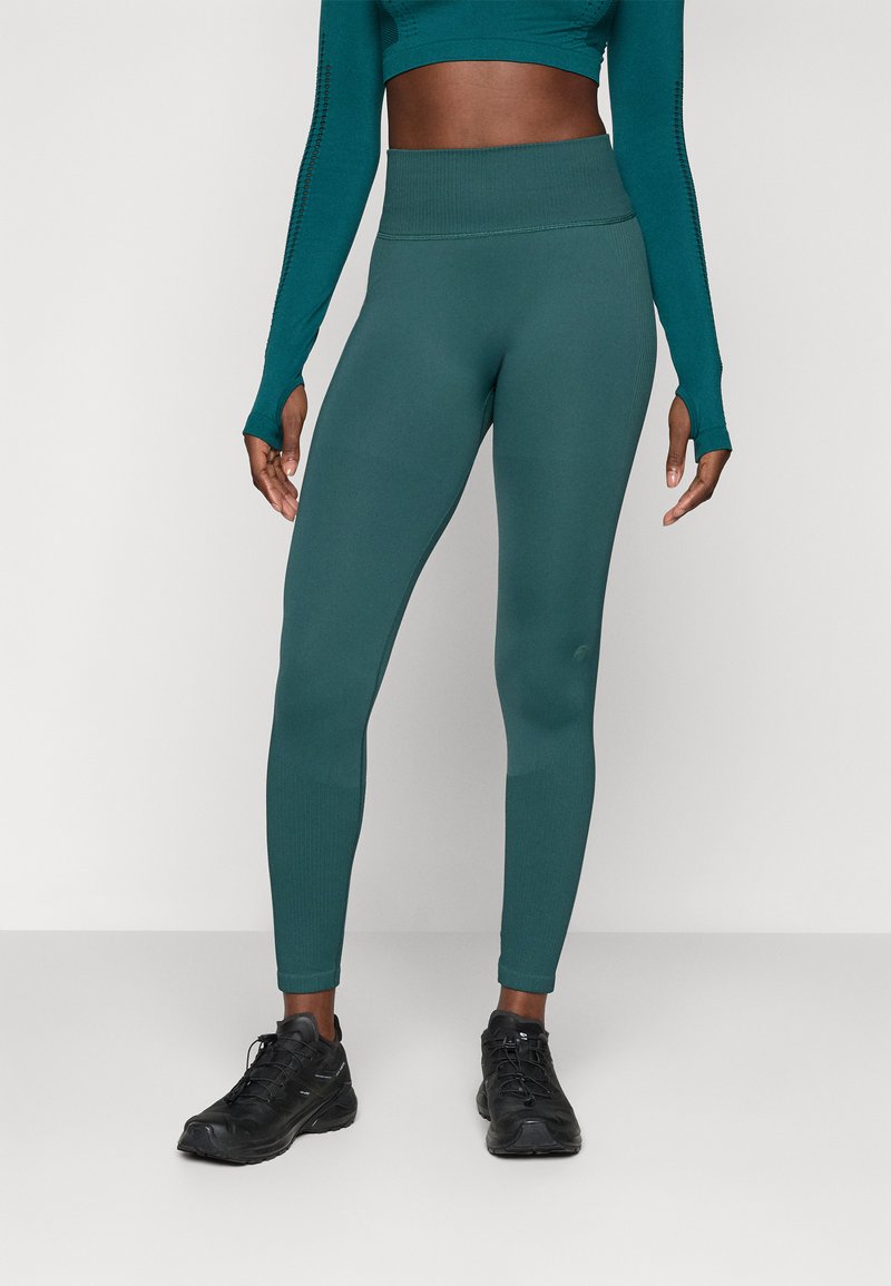 Leggings deportivos color verde azulado con cintura alta, textura suave y costuras mínimas, combinados con zapatillas negras.