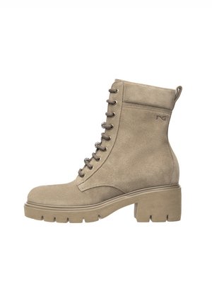 Bottines en suède beige avec un talon plat et épais, un laçage à l'avant et une languette à l'arrière. Présente des coutures renforcées sur les côtés.