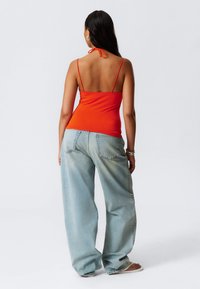 Top rosso senza maniche con spalline sottili, legato al collo, abbinato a jeans a gamba larga blu chiaro. Tessuto morbido, vestibilità casual.
