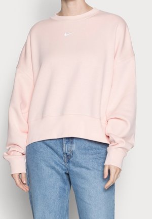 Rosa Sweatshirt mit Rundhalsausschnitt, oversized Fit, überschnittenen Schultern und einem weißen Nike-Logo auf der Brust, kombiniert mit hellblauen Jeans.